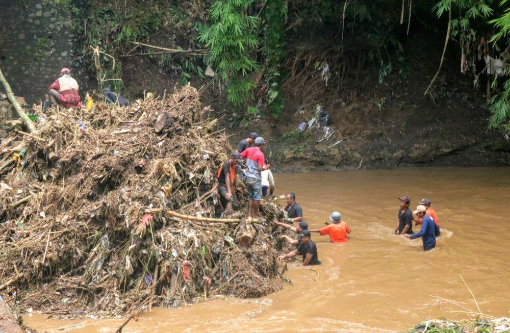 Warga bergotong royong membersihkan sampah yang menyangkut di tiang bawah jembatan. IDN Times/ Alfi Ramadana