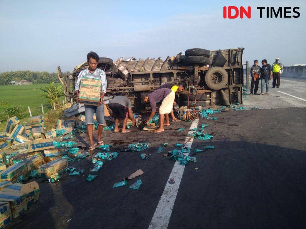 Sejumlah warga membantu mengevakuasi kecap dalam kardus yang tumpah setelah mobil boks pengangkutnya terguling di jalan tol ruas Kertosono - Ngawi wilayah Kabupaten Madiun, Sabtu (2/5). IDN Times/Nofika Dian Nugroho