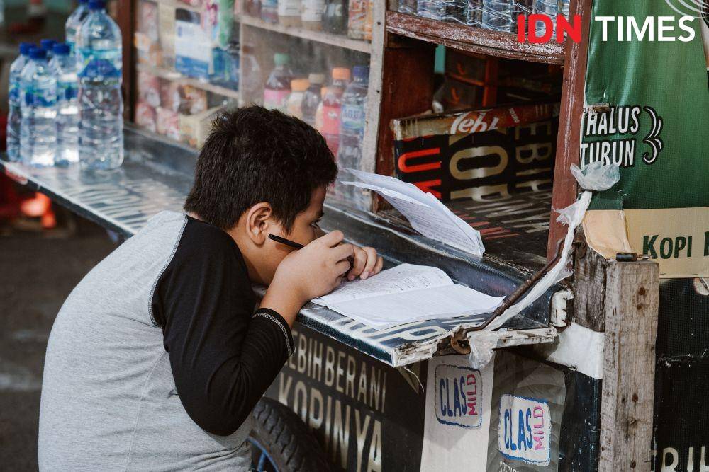 Seorang anak terlihat sedang belajar sambil menunggu Warung Kaki Lima yang menjual minuman di sekitar Kota Tua, Jakarta Barat pada Rabu (5/8/2020) (IDN Times/Aldila Muharma)