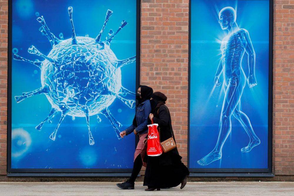Warga berjalan melewati ilustrasi virus di luar pusat sains regional, saat kota dan daerah sekeliling menghadapi larangan lokal sebagai upaya menghindari 'lockdown' secara lokal yang diberlakukan di wilayah tersebut, di tengah penyebaran penyakit virus korona (COVID-19) di Oldham, Britain, Senin (3/8/2020) (ANTARA FOTO/REUTERS/Phil Noble)