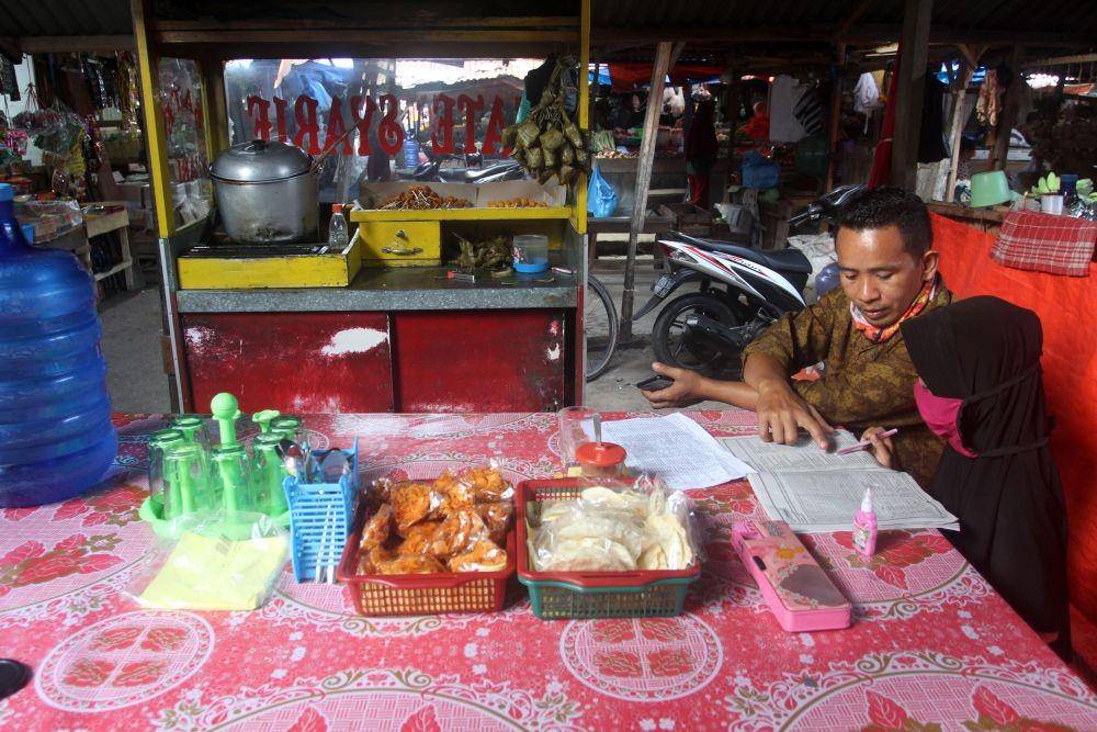 Pedagang sate, Adral membimbing anaknya Hanifah mengerjakan tugas sekolah sambil berjualan di pasar Tabing, Padang, Sumatera Barat, Jumat (14/8/2020) (ANTARA FOTO/Muhammad Arif Pribadi)