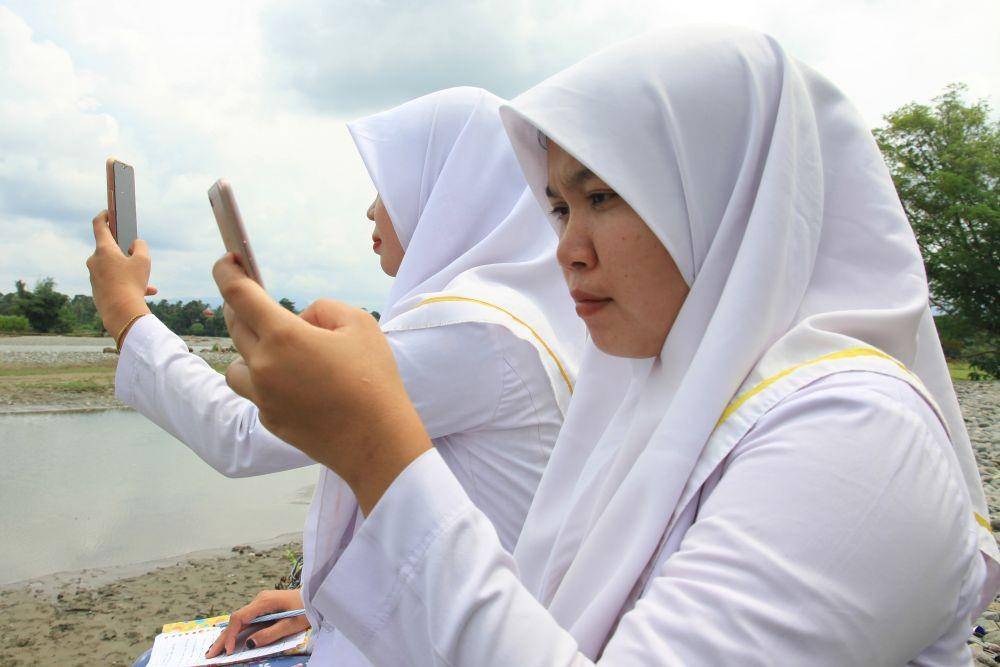 (Mahasiswi keperawatan mengikuti proses belajar mengajar dalam jaringan (daring) di pinggir sungai Sikundo supaya bisa mendapat sinyal di Desa Keutambang, Pante Ceureumen, Aceh Barat, Aceh, Rabu (26/8/2020)) ANTARA FOTO/Syifa Yulinnas