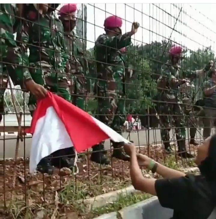 Seorang wanita serahkan bendera merah putih pada TNI di tengah demo/@infokomando