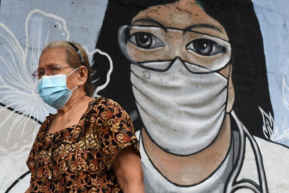 Seorang perempuan memakai masker pelindung sebagai pencegahan terhadap penyakit virus korona (COVID-19) berjalan melewati mural yang didedikasikan kepada pekerja yang berada di garis depan, di Manila, Filipina, Senin (11/1/2021) (ANTARA FOTO/REUTERS/Lisa Marie David)