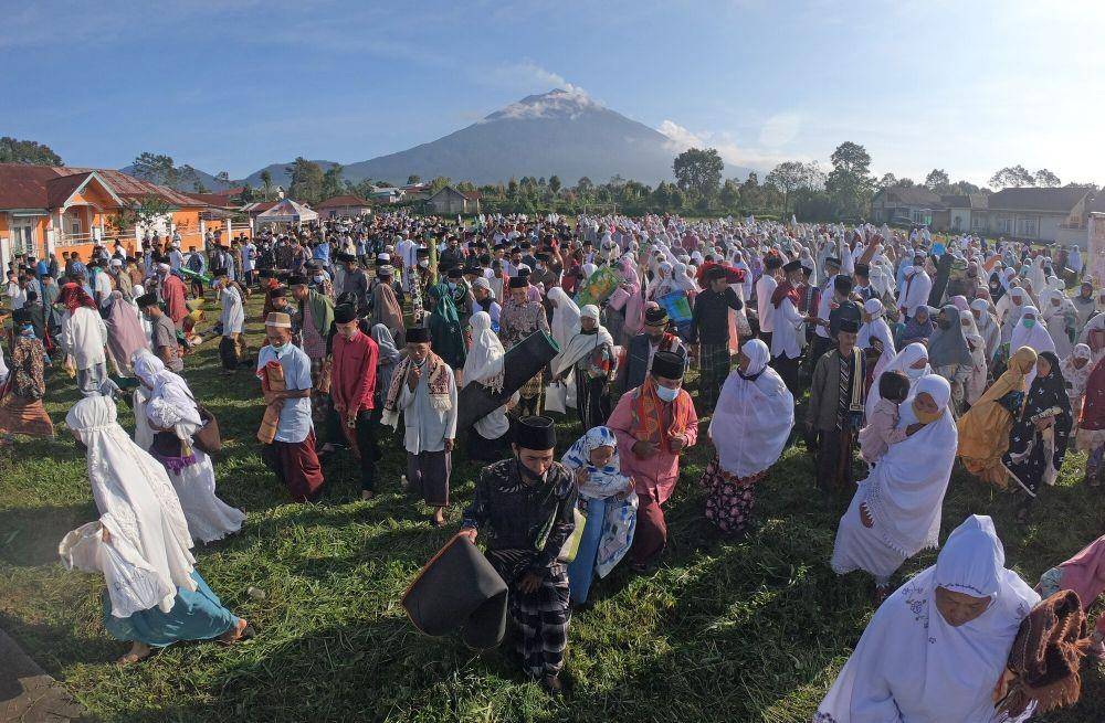Umat muslim beranjak pulang sambil membawa alas shalat usai menunaikan shalat Idul Fitri 1442 Hijriah di lapangan Gunung Labu dengan latar belakang Gunung Kerinci, Kayu Aro Barat, Kerinci, Jambi, Kamis, 13 Mei 2021. (ANTARA FOTO/Wahdi Septiawan)
