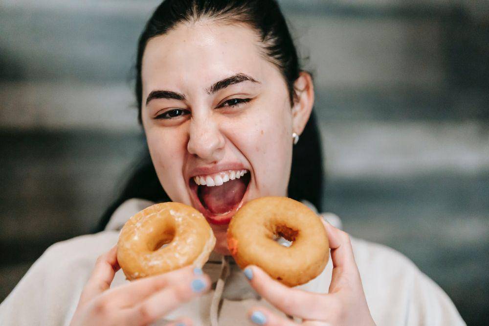 hungry woman with delicious donuts at home (pexels/Andres Ayrton)