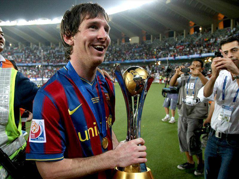Messi tersenyum sambil memegang trofi Piala Dunia Antarklub (goal.com)