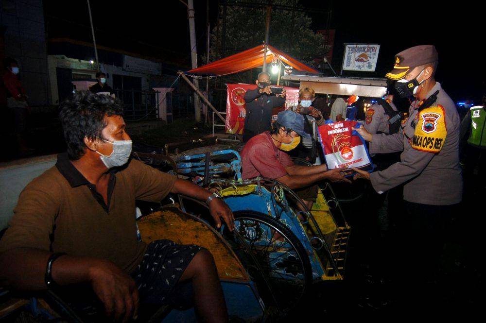 Personel polisi menyerahkan bantuan sembako kepada pengayuh becak saat patroli skala besar di Kabupaten Tegal, Jawa Tengah, Jumat (23/7/2021) malam (ANTARA FOTO/Oky Lukmansyah)