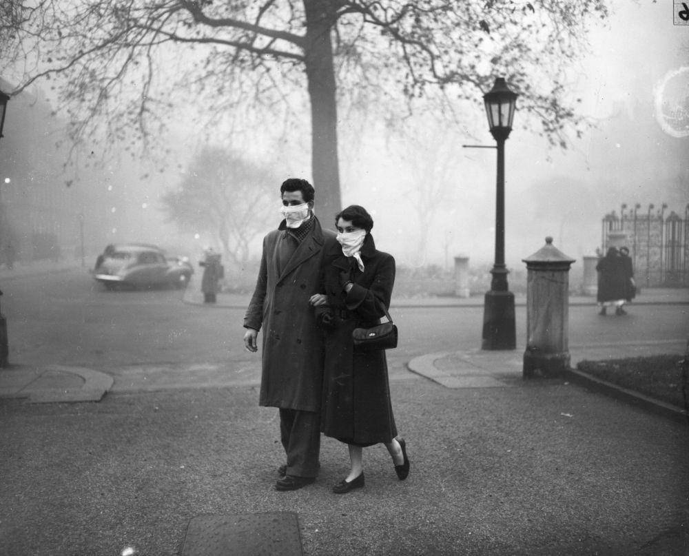 Sepasang suami istri berjalan di London mengenakan masker selama kabut asap pada November 1953 di London. (flashbak.com/Monty Fresco)