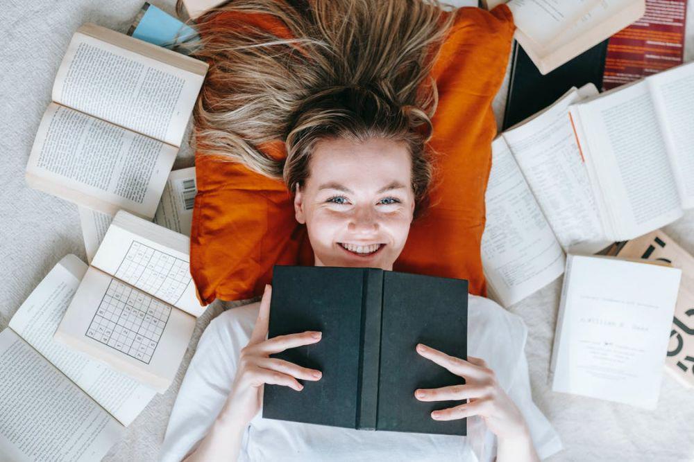 Ilustrasi seorang wanita tersenyum dikelilingi dengan buku (Pexels.com/George Milton)