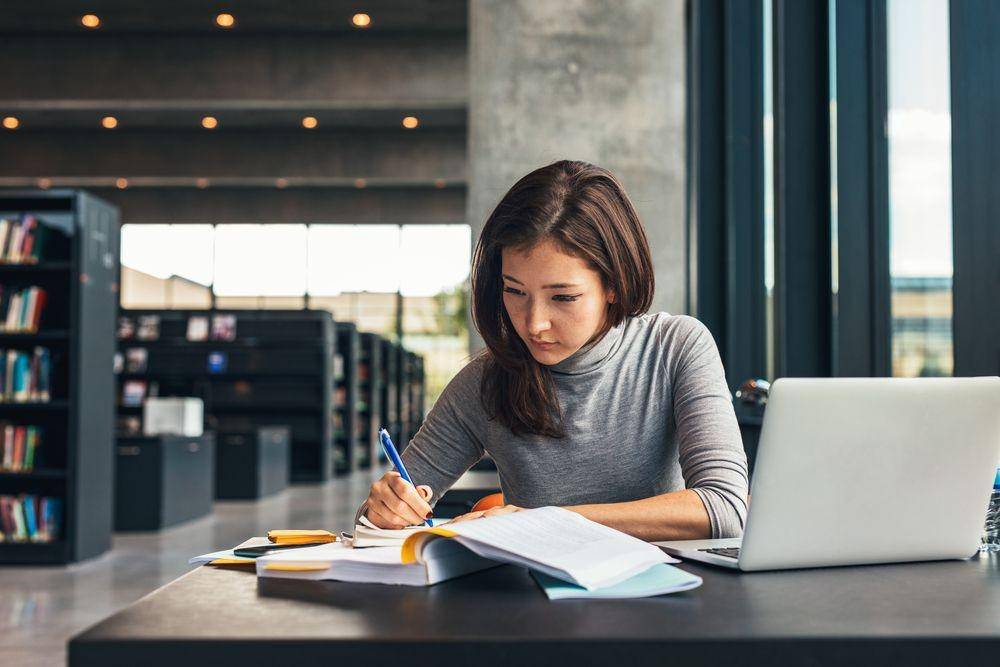 Seorang cewek sedang menulis di perpustakaan (Shutterstock/Jacob Lund)