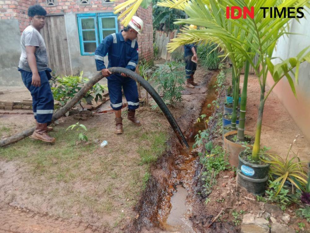 Petugas dari Pertamina EP 1 Jambi membersihkan minyak mentah yang mengalir ke rumah warga (IDN Times)