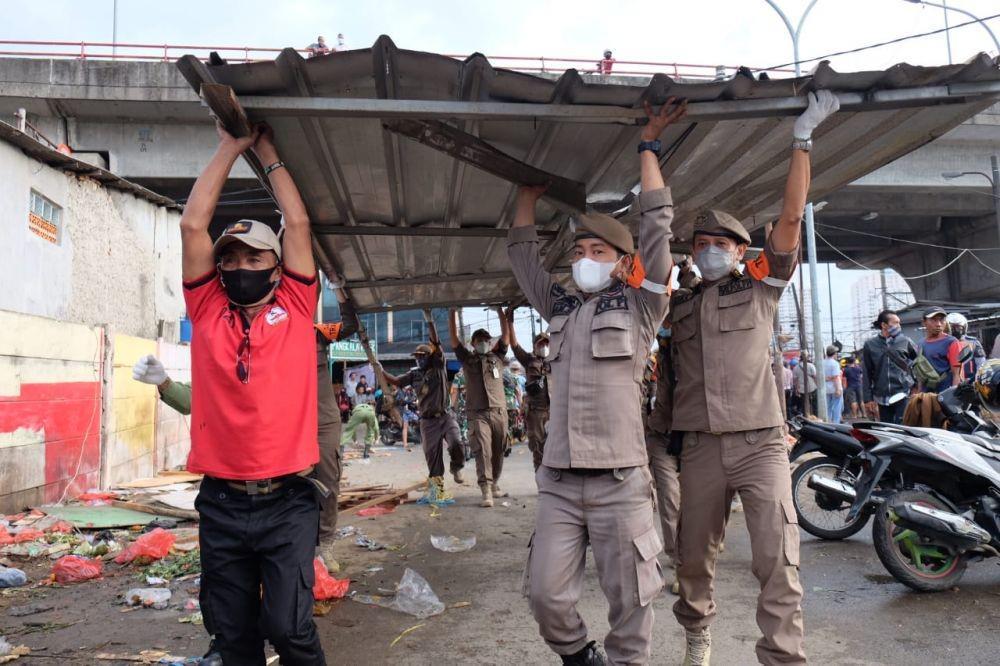 Anggota Satpol PP Kota Depok mengangkat bagian atas penutup bangunan yang digunakan PKL untuk berjualan. (Istimewa)