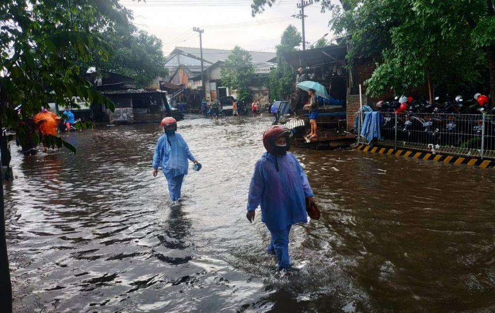 Dua warga berjalan kaki melintasi jalan yang tergenang air. IDN Times/Alfi Ramadana