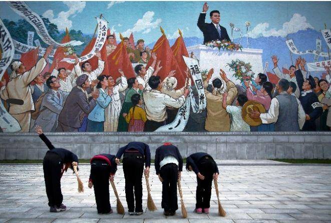 Warga Korea Utara memberi hormat ke mural yang menunjukkan mendiang pemimpin Korea Utara Kim Il Sung, sebelum menyapu area sekitar mural ini pada Selasa, 1 Desember 2015, di Pyongyang, Korea Utara. (dok. AP Photo/Wong Maye-E)