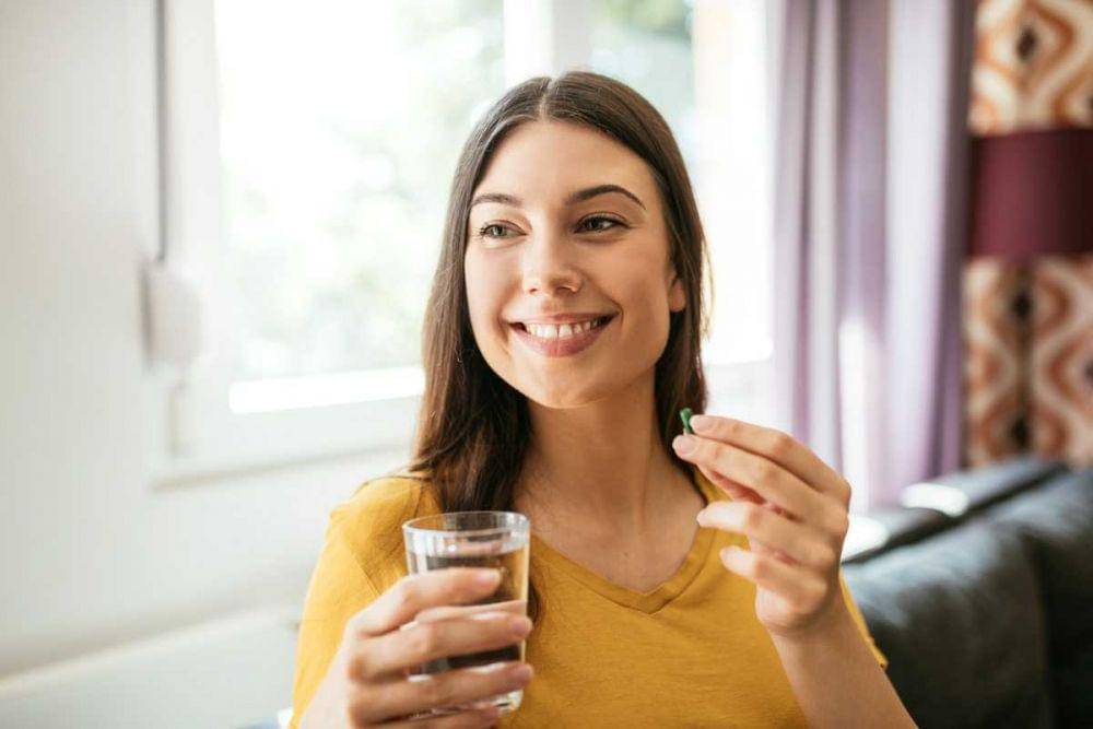 Seorang perempuan minum suplemen dengan segelas air putih.
