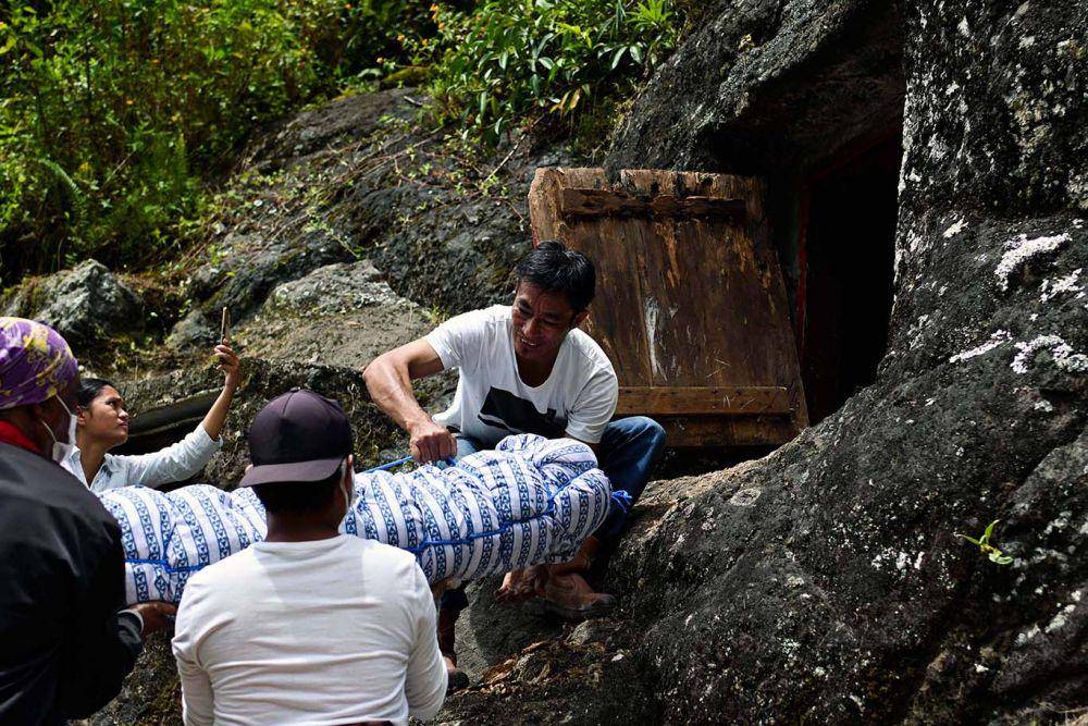 Keluarga memasukkan kembali mayat pada liang setelah dilakukan pembersihan dan penggantian baju pada acara ritual Manene di Lembang Benteng Kado, Kecamatan Kapala Pitu, Kabupaten Toraja Utara, Sulawesi Selatan, Selasa (16/8/2022). Moh Niaz Sharief/bt