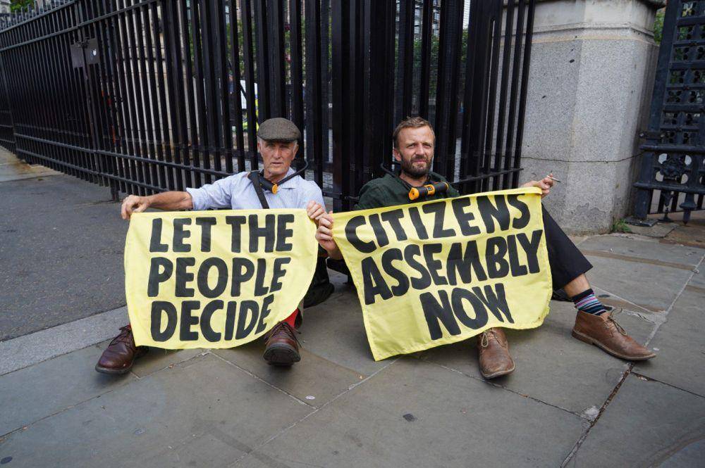 Dua aktivis Extinction Rebellion Inggris pada 2 September 2022 mengunci leher mereka ke pagar di gedung parlemen. (Twitter.com/Extinction Rebellion UK)