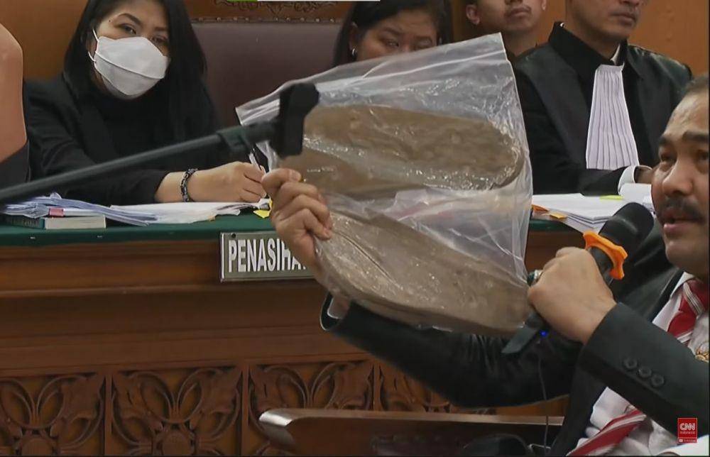 Pengacara Brigadir J, Kamaruddin Simanjuntak menunjukkan sandal sebagai bukti saat sidang pada Selasa (1/1/2022). (youtube.com/CNN Indonesia TV POOL)