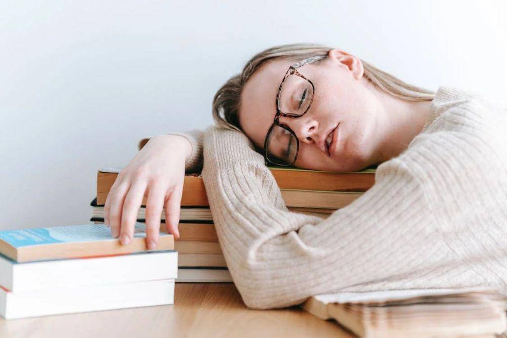 ilustrasi seorang perempuan tertidur di atas tumpukan buku (pexels.com/George Milton)