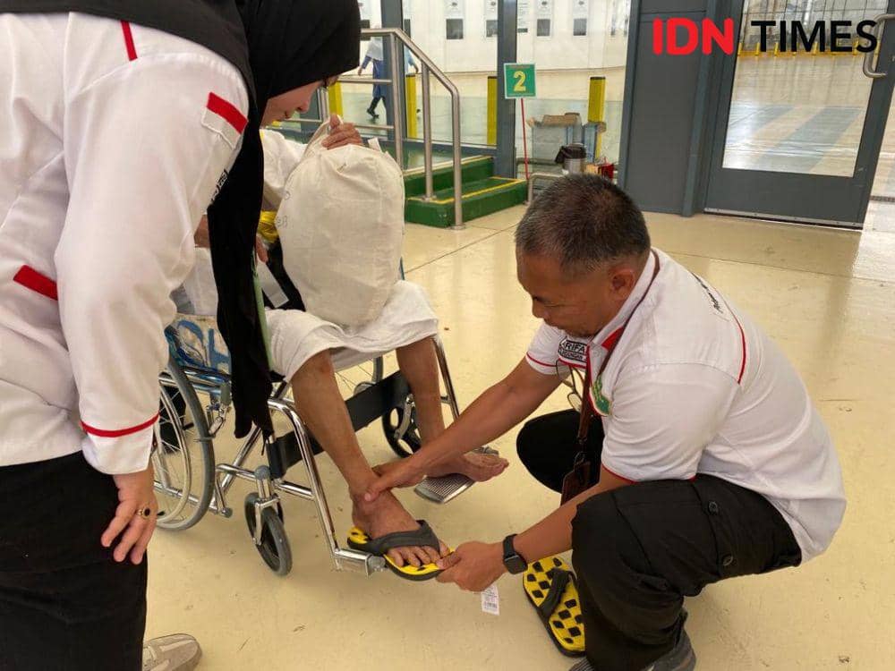 Petugas memakaikan sendal kepada jemaah haji yang tidak menggunakan alas kaki.