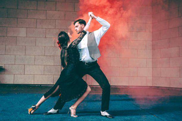Pasangan muda yang  menari tango di atas panggung dengan bom asap merah di latar belakang (istockphoto.com/LordHenriVoton)