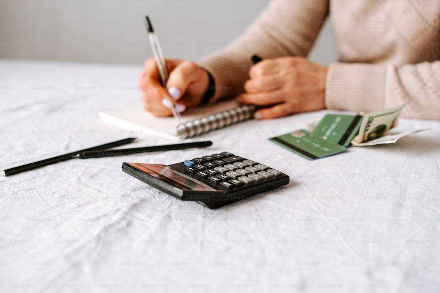 seseorang menulis dibuku catatan disebelah kalkulator (Unsplash.com/Unsplash+)