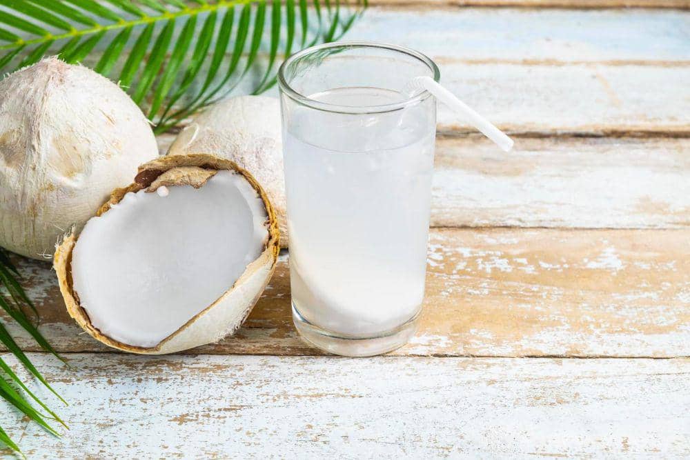 Ilustrasi segelas air kelapa segar dengan potongan kelapa hijau dan sedotan di latar berwarna cerah.