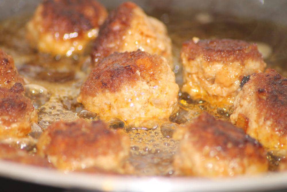 Ilustrasi chicken tsukune berbentuk bulat sedang digoreng dalam wajan berisi minyak panas hingga kecokelatan.