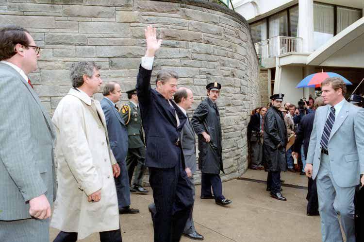 Presiden AS, Ronald Reagan, melambai sebelum dia ditembak di luar Hotel Washington, Senin, 30 Maret 1981. Di sisi kiri, ada agen Dinas Rahasia bernama Jerry Parr dengan jas abu-abu. Ia mendorong Reagan ke dalam limusin. Lalu, ada agen dinas rahasia Timothy J McCarthy tertembak di perutnya, yang berada di depan Ronald Reagan. (commons.wikimedia.org/Michael Evans)