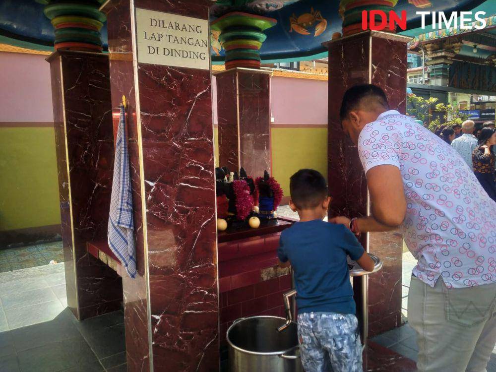 Seorang bapak yang menuntun anaknya melakukan ritual di Kuil Shri Mariamman dalam momen Deepavali (IDN Times/Eko Agus Herianto)