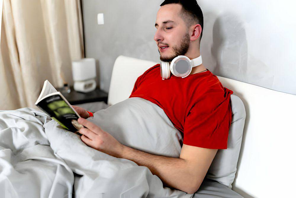 ilustrasi pria menggunakan bantal dan selimut ketika membaca (istockphoto.com/ProfessionalStudioImages)