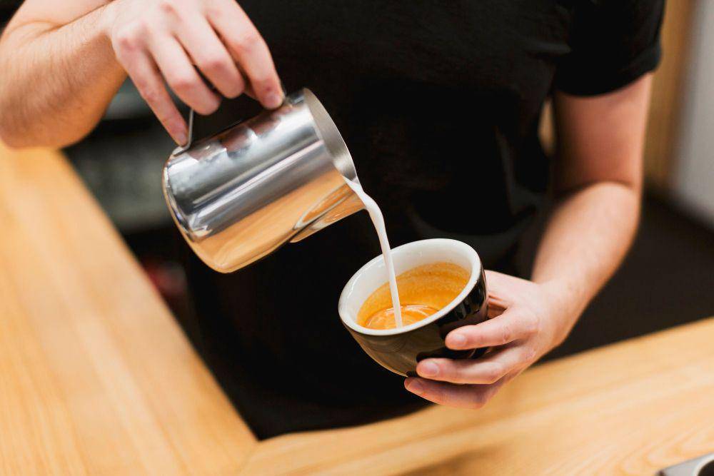 ilutrasi barista menuangkan susu ke dalam cangkir berisi espresso (freepik.com/freepik)