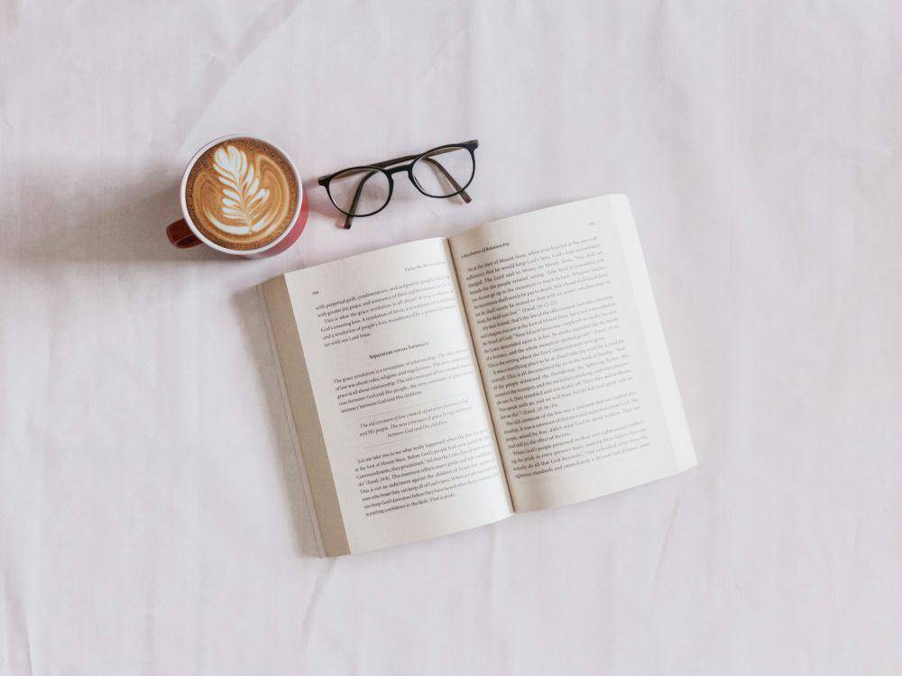 Sebuah buku di dekat kacamata dan kopi cappuccino (unsplash.com/Sincerely Media)