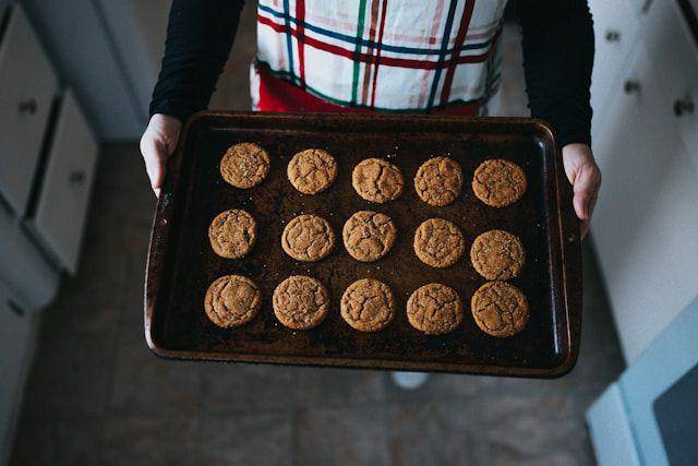 ilustrasi seseorang yang membawa keluar loyang berisi kue kering dari oven (unsplash.com/Nathan Dumlao )