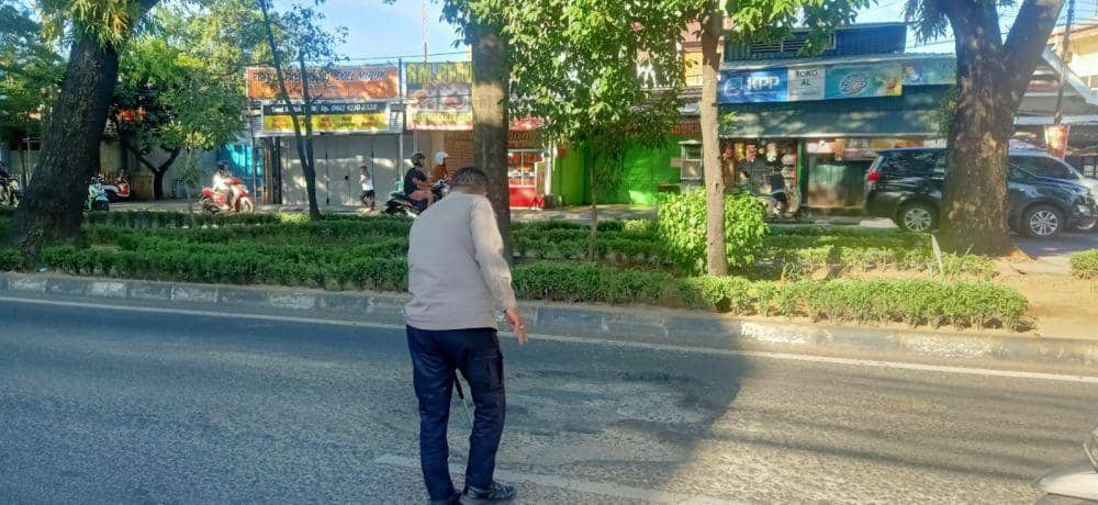 Seorang petugas kepolisian mengukur kedalaman lubang di Jalan Hertasning Makassar. (Dok. Istimewa)