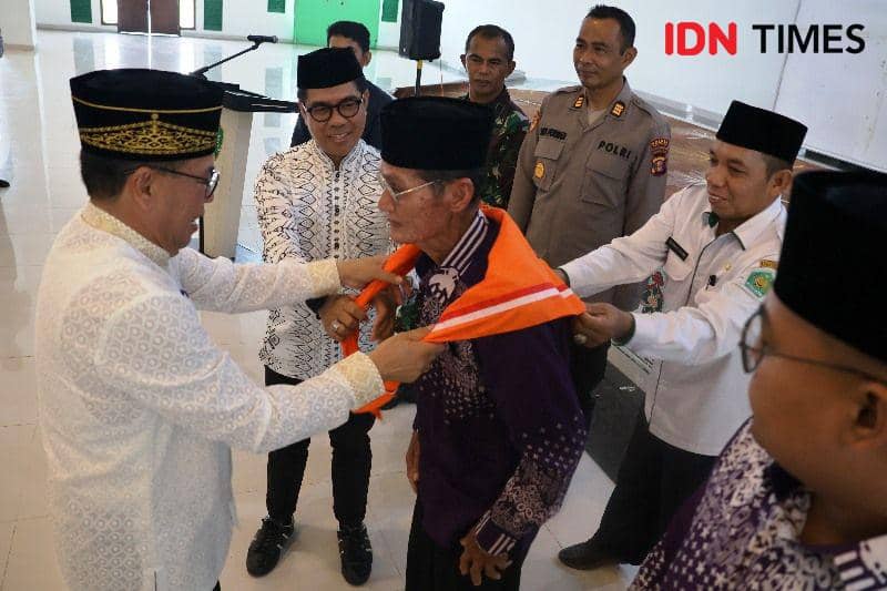 Pj Bupati PPU, Makmur Marbun memasangkan syal simbol pelepasan Calhaj pada jamaah tertua (IDN Times/Ervan)
