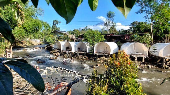 Suasana Dusun Camp Riverside Glamping, area glamping di tepi sungai yang dikelilingi lingkungan alami.