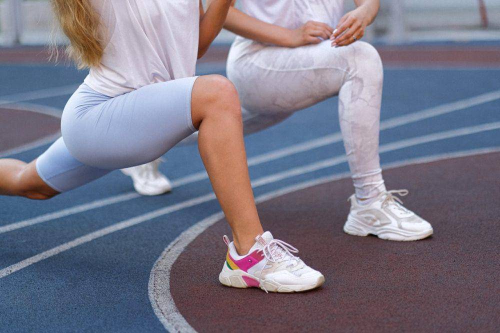 Dua orang perempuan sedang melakukan latihan lunges.