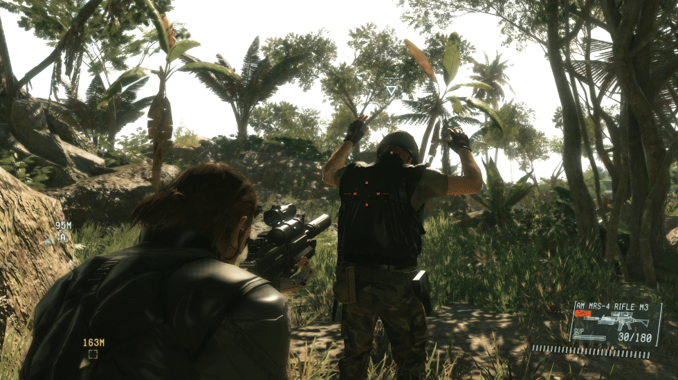 Karakter utama mengarahkan senjata ke musuh yang menyerah di tengah hutan tropis dalam gameplay Metal Gear Solid V: The Phantom Pain.