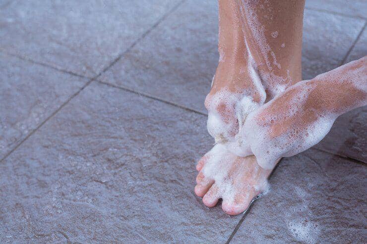 Tangan membasuh kaki perempuan dengan sabun saat perawatan spa, dengan kaki direndam dalam wadah berisi air.