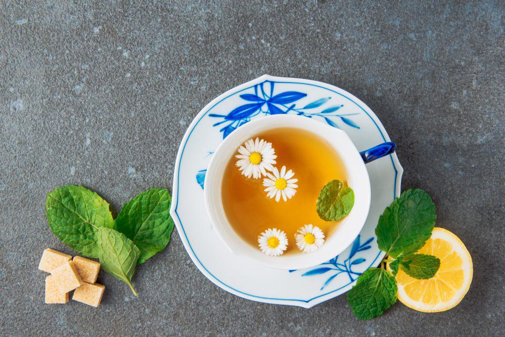 Tea of chamomile in a cup and saucer with lemon, brown sugar cubes and green leaves (Image by 8photo on Freepik)