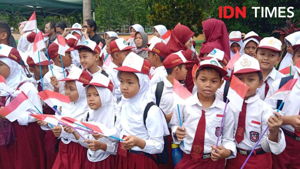 Para siswa menyambut di sepanjang jalan sambil membawa bendera Merah Putih dan tulisan dukungan untuk Presiden Prabowo. (IDN Times/Fariz Fardianto)