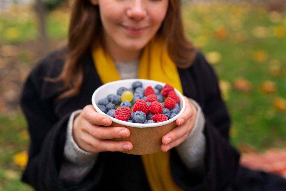 Perempuan membawa mangkok berisi aneka buah berry.