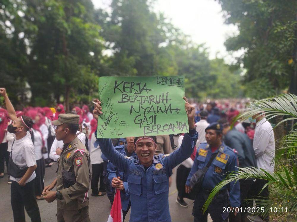 Salah seorang tenaga honorer membawa poster protes (IDN Times/Ruhaili)