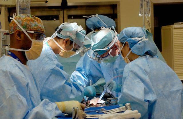 Tim dokter berseragam bedah melakukan operasi di ruang operasi sebagai ilustrasi penanganan kanker tulang.