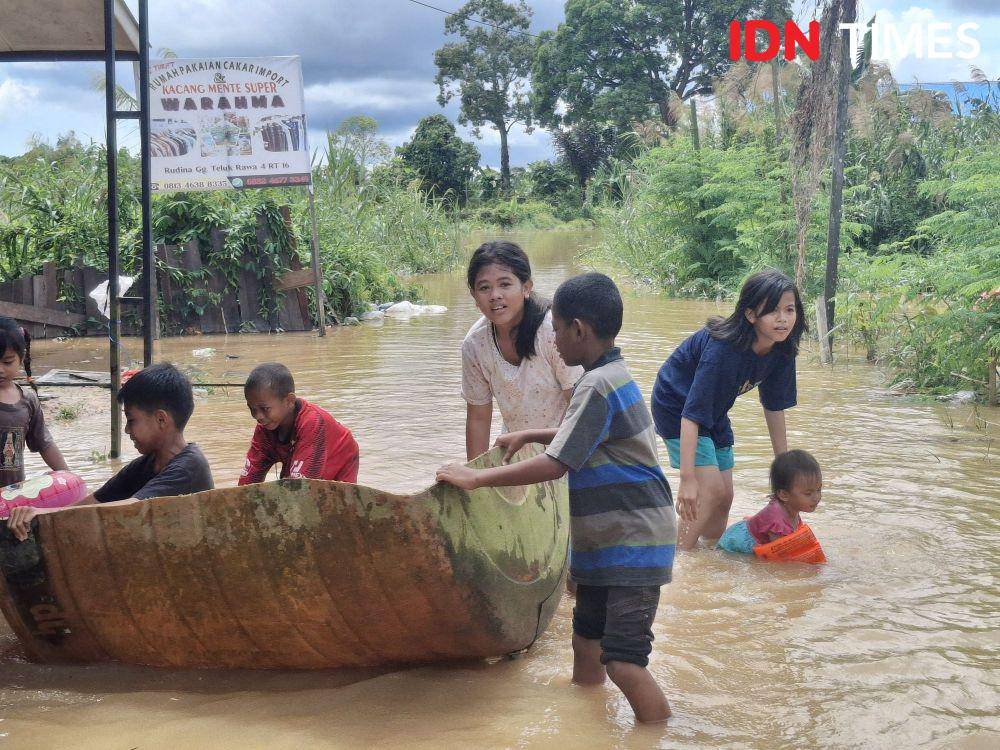 Sejumlah anak bermain di tengah banjir di Dusun Teknik, Desa Masabang Sangatta Selatan, Kutai Timur, Minggu (26/1/2025) kemarin. Meski kerap muncul buaya saat banjir, warga mengaku tak takut. (IDN Times/Erik Alfian)