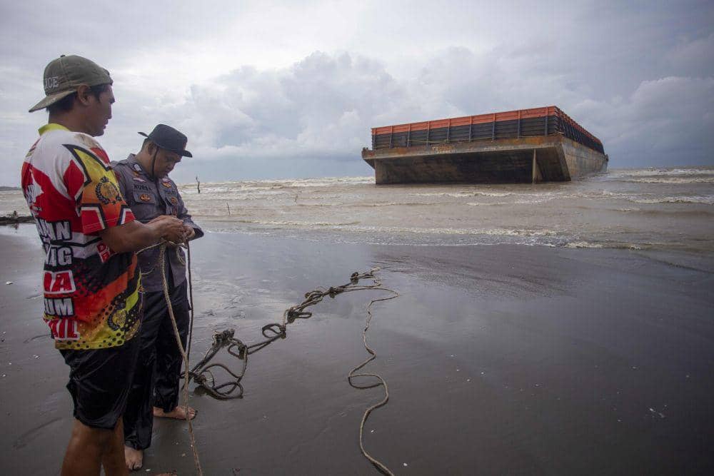 Personel polisi dibantu warga berusaha mengikat tongkang yang terdampar di bibir Pantai Tiris, Pasekan, Indramayu, Jawa Barat, Senin (20/1/2025).   ANTARA FOTO/Dedhez Anggara/tom
