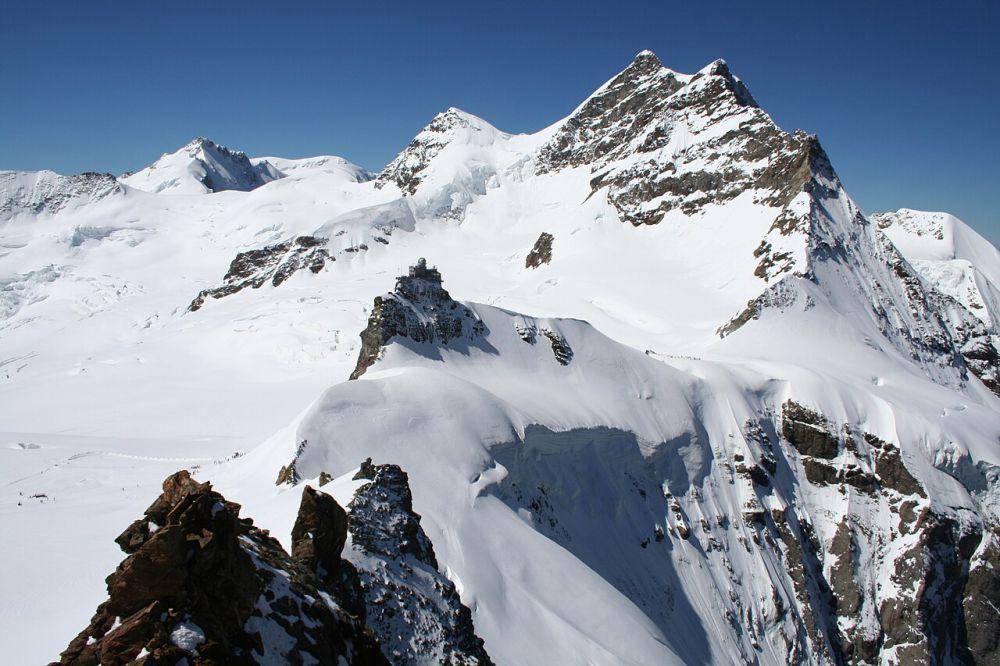 Gunung Jungfrau dilihat dari Gunung Monch dengan punggungan bukit Jungfrouch yang menghubungkan Gunung Monch dan Gunung Jungfrau serta Observatorium Astronomi Sphinx di tengahnya (commons.wikimedia.org/Pmau)