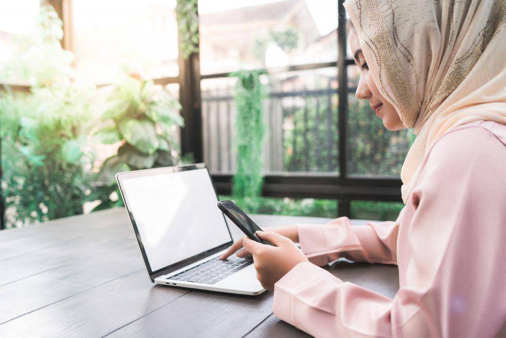 Ilustrasi perempuan mengecek HP dan laptop. (Freepik / tirachardz)